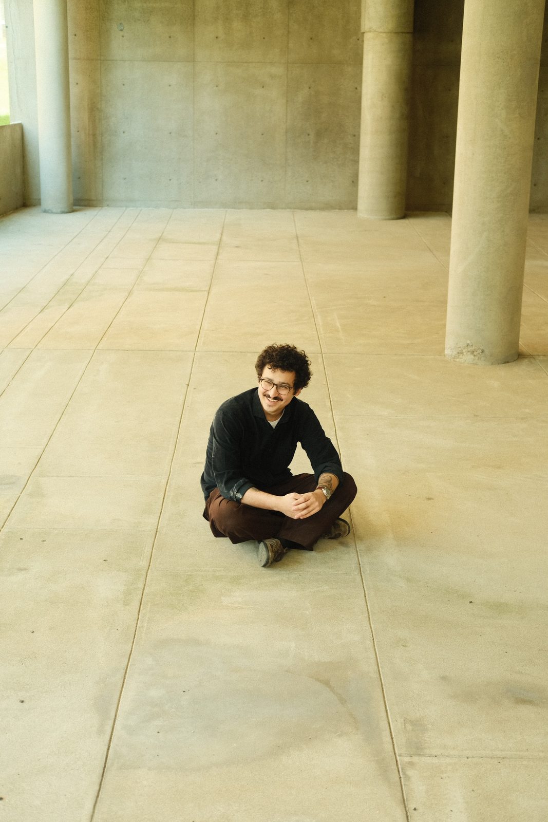 Edu Herédia seated on the floor of a concrete hall