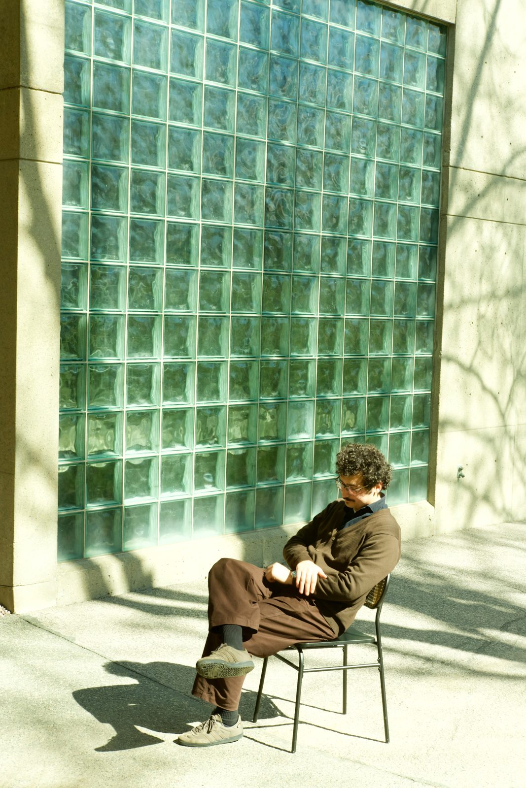 Edu Herédia seated before a glass-block wall in dappled light